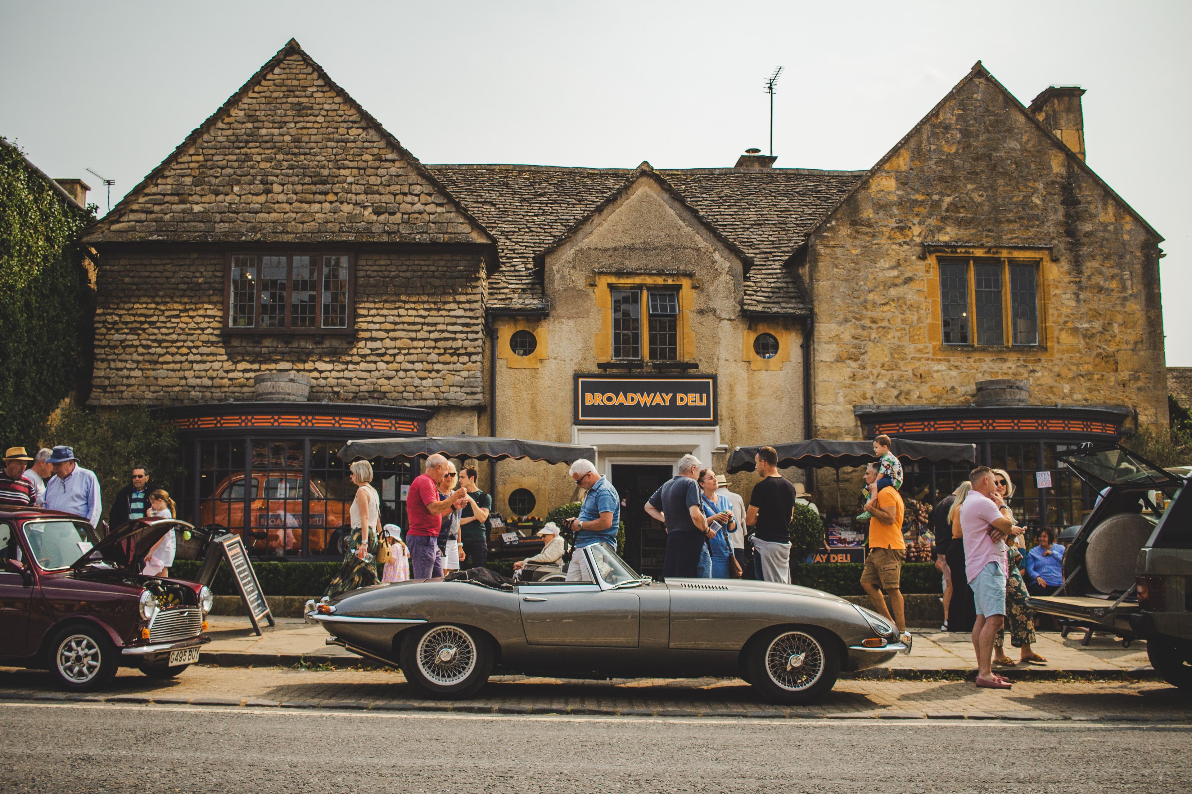 A street scene with vintage cars and people outside Broadway Deli